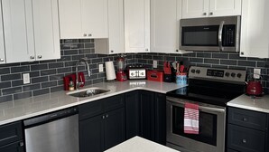 A modern kitchen with white cabinets, black countertops, a stainless steel dishwasher, a microwave, a toaster, and a kettle. - Townhouse in Old Fishtown! 10 mins to Center City & Stadiums (Philadelphia)