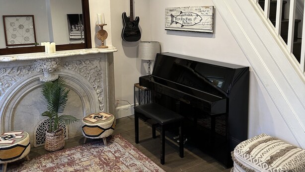 A living room with a fireplace, a piano, a staircase, and a wall-mounted sign. - Townhouse in Old Fishtown! 10 mins to Center City & Stadiums (Philadelphia)