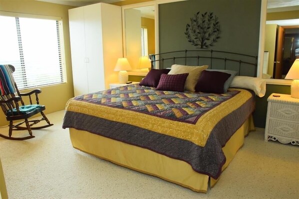 Un dormitorio con una cama grande, un sillón mecedora, una mesita de noche y un aparador.
