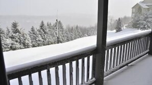 Un balcon enneigé avec une balustrade, donnant sur un paysage recouvert de neige et une maison.