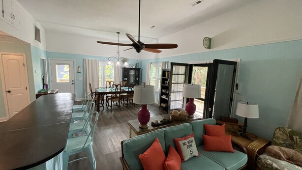 A spacious living area with a dining table, a sofa with cushions, a ceiling fan, and a kitchen area with a bar counter. - "MUCK IT"-QUINTESSENTIAL Edisto Beach House w/in Steps of Beach (Edisto Island)