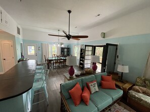 A spacious living area with a dining table, a sofa with cushions, a ceiling fan, and a kitchen area with a bar counter. - "MUCK IT"-QUINTESSENTIAL Edisto Beach House w/in Steps of Beach (Edisto Island)