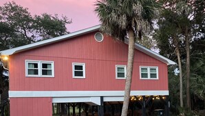 A red building with a covered patio area, a palm tree, and a gravel driveway. - "MUCK IT"-QUINTESSENTIAL Edisto Beach House w/in Steps of Beach (Edisto Island)