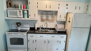 A kitchen with white cabinets, a stove, a sink, and a refrigerator. There is a sign on the wall that reads "EDISTO BEACH". - "MUCK IT"-QUINTESSENTIAL Edisto Beach House w/in Steps of Beach (Edisto Island)