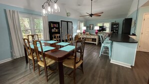 A spacious dining area with a wooden table and chairs, a ceiling fan, and a kitchen area with a TV and cabinets. - "MUCK IT"-QUINTESSENTIAL Edisto Beach House w/in Steps of Beach (Edisto Island)