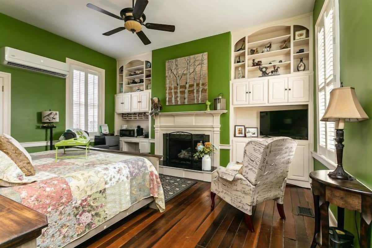 A bedroom with a bed, a chair, a fireplace, and built-in shelving.