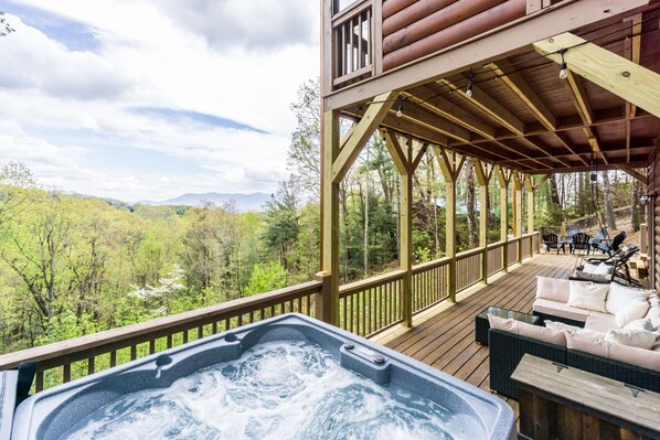 A wooden deck with a hot tub, outdoor seating, and a view of a forested valley. - Mountain getaway with breathtaking views. Pet Friendly! (Ellijay)