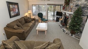A cozy living room with a brown sofa, a wooden coffee table, a green armchair, and a fireplace with a Christmas tree. - Seven Springs 2 BR Deluxe Condo with Mountain Views by RedAwning (Champion)