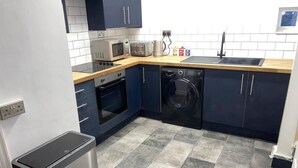 Une cuisine compacte avec des meubles de couleur bleu foncé, un four à micro-ondes, un grille-pain, une bouilloire et un lave-linge.