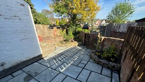 Une terrasse dallée avec des carreaux de pierre, entourée d’un mur de briques et d’une clôture en bois.
