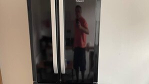 A black refrigerator with a double door and a freezer drawer, placed next to a trash bin. - Commuters Getaway Chesterfield (Chesterfield)