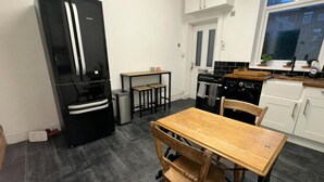 A compact kitchen with a black refrigerator, a wooden dining table, and a window. - Commuters Getaway Chesterfield (Chesterfield)