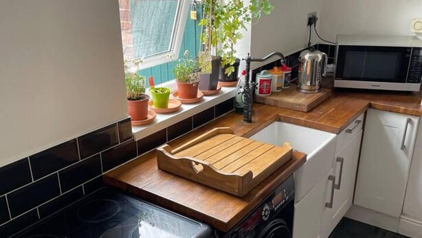 A kitchen with a black stove, white cabinets, a wooden cutting board, and potted plants on the windowsill. - Commuters Getaway Chesterfield (Chesterfield)