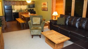 A cozy living area with a sofa, armchair, and coffee table, a dining table with chairs, and a kitchen in the background. - Seven Springs 3 BR Condo, walk to slopes! by RedAwning (Champion)