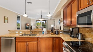 A modern kitchen with wooden cabinets, stainless steel appliances, granite countertops, and pendant lighting.