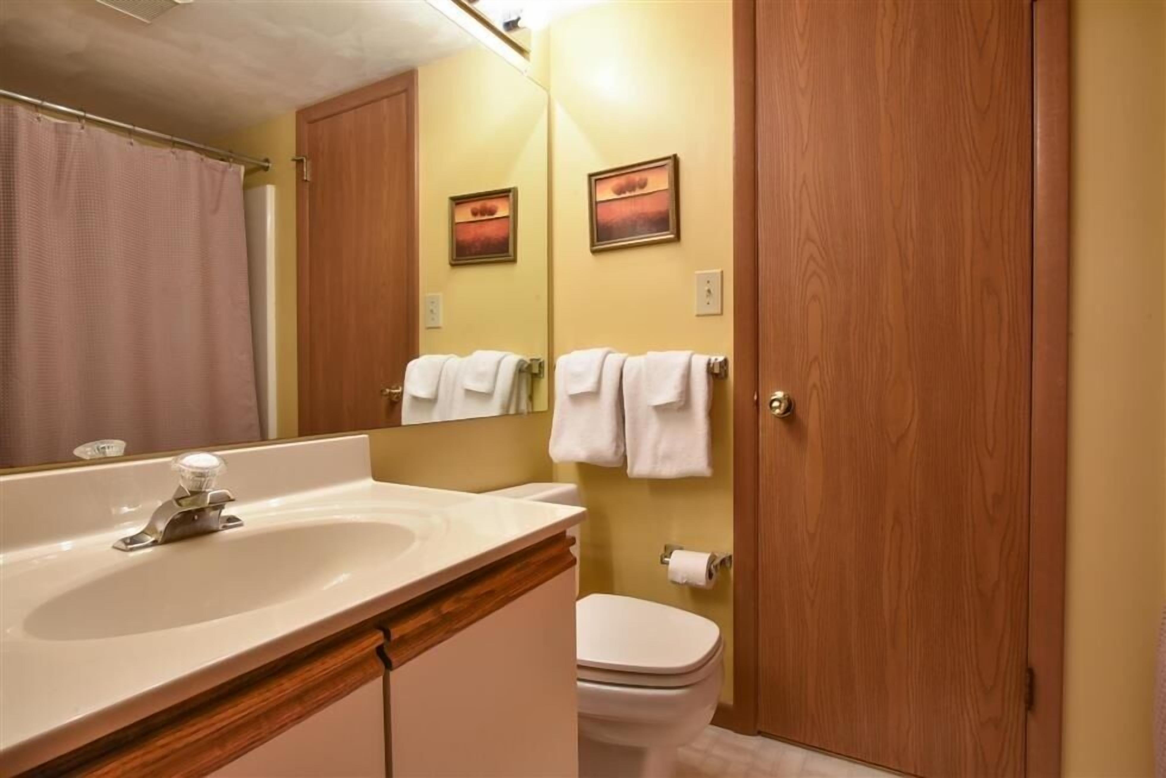 Ein Badezimmer mit Waschbecken, Spiegel, Toilette und Holztür.