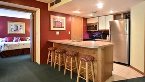A compact kitchen with a central island, bar stools, a refrigerator, and a microwave.