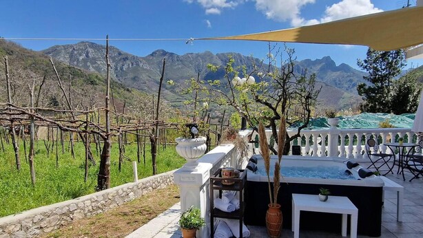 Une terrasse avec vue sur les montagnes, une table blanche, des chaises et un petit jacuzzi.