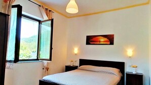 Une chambre à coucher comprenant un lit, deux tables de chevet, une fenêtre avec des rideaux, un luminaire fixé au mur et un tableau.