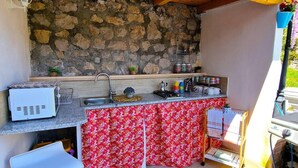 Une cuisine compacte avec un mur en pierre, un petit évier et un plan de travail sur lequel sont disposés divers objets.