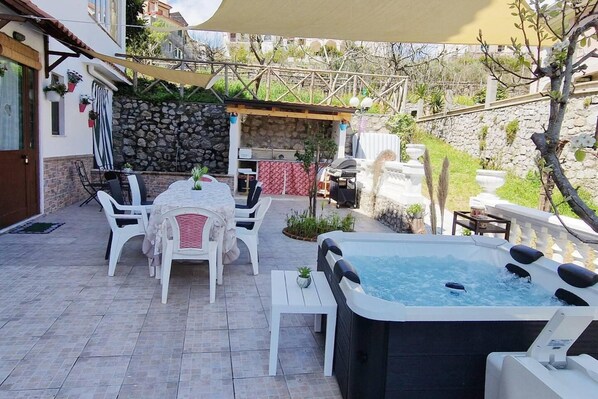 Un patio con mobiliario exterior, un jacuzzi y un muro de piedra.