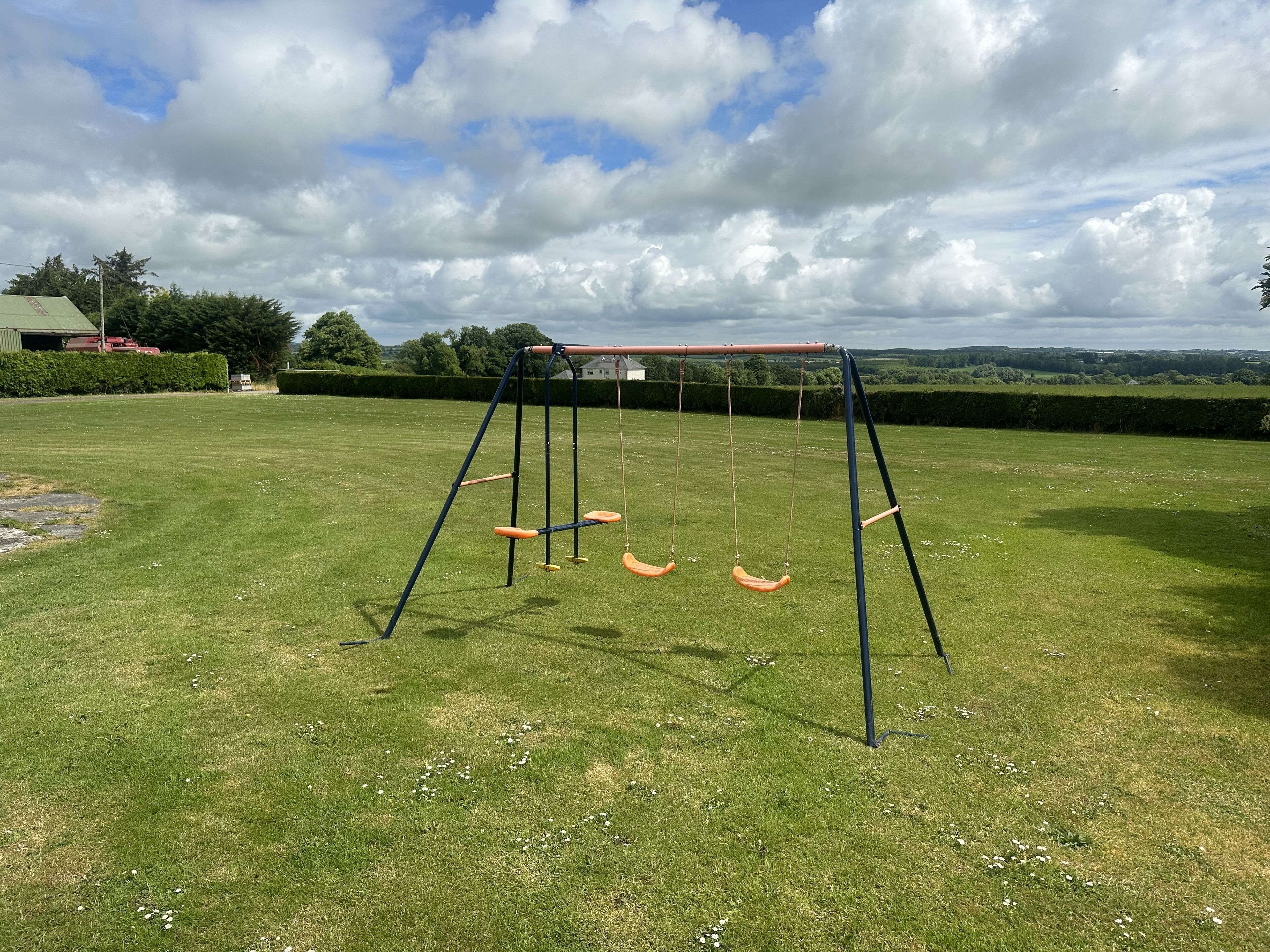 A swing set in a grassy yard with a house and trees in the background.