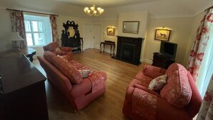 A spacious living room with a fireplace, two red sofas, a chandelier, and a television. - Beautiful Irish Farmhouse an Hours Drive From Four Irish Cities (Clonmel)