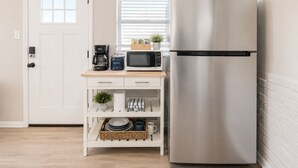 Een kleine keuken met een roestvrijstalen koelkast, een magnetron en een koffiezetapparaat op een houten aanrecht.