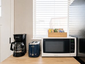 Een kitchenette met een koffiezetapparaat, broodrooster en magnetron op een houten aanrecht.