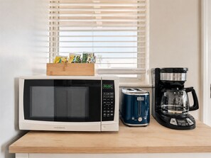 Une cuisine équipée d’un four à micro-ondes, d’un grille-pain et d’une machine à café, le tout posé sur un plan de travail en bois.
