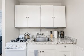 A compact kitchen with white cabinets, a stainless steel sink, a gas stove, and a kettle. - Beach Loft 32 Steps From the Sand (Ventura)