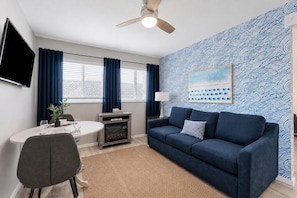 A modern living room with a blue sofa, a dining table, and a fireplace. - Beach Loft 32 Steps From the Sand (Ventura)