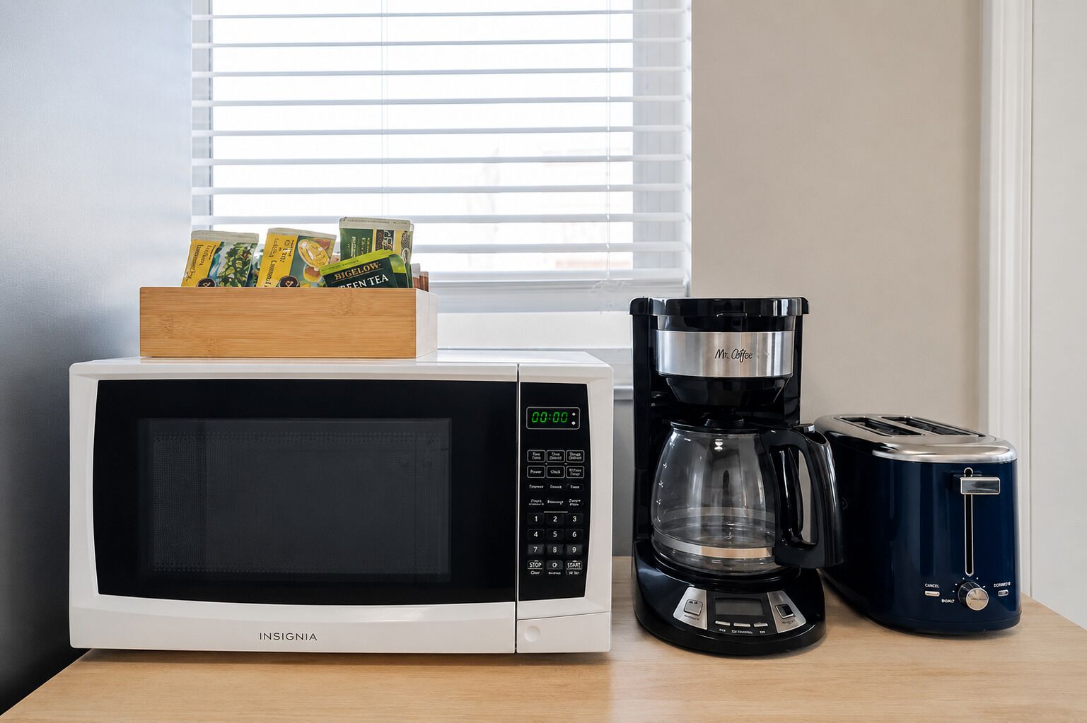 Una cocina con microondas, cafetera y tostadora sobre una mesa de madera.