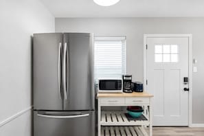 A compact kitchen with a stainless steel refrigerator, a microwave, a coffee maker, and a small wooden table. - Beach Loft 32 Steps From the Sand (Ventura)