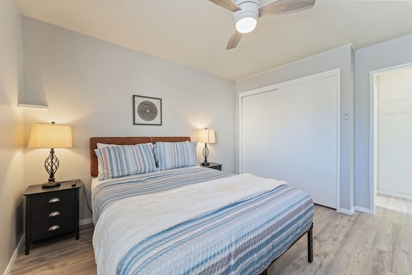 A bedroom with a bed, two bedside tables with lamps, a ceiling fan, a framed picture on the wall, and a closet.