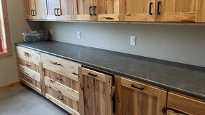 A kitchen with wooden cabinets, a grey countertop, and a window with blinds. - Peaceful Farmhouse with hot tub (Yankton)