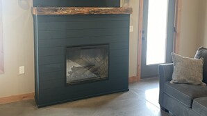 A living room with a fireplace, a television mounted above it, and a couch with pillows. - Peaceful Farmhouse with hot tub (Yankton)