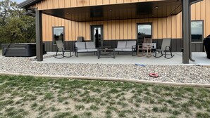 A modern building with a covered patio area featuring outdoor seating and a grill. - Peaceful Farmhouse with hot tub (Yankton)
