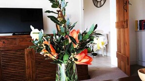 Ett vardagsrum med ett träbord, en vas med blommor, en tv och en klocka på väggen.