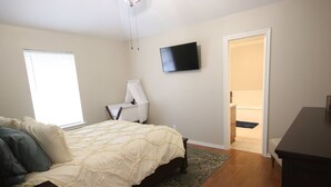 A bedroom with a bed, a TV mounted on the wall, and a door leading to a bathroom. - Royal Entertainer - STAYeasttexas (Chandler)