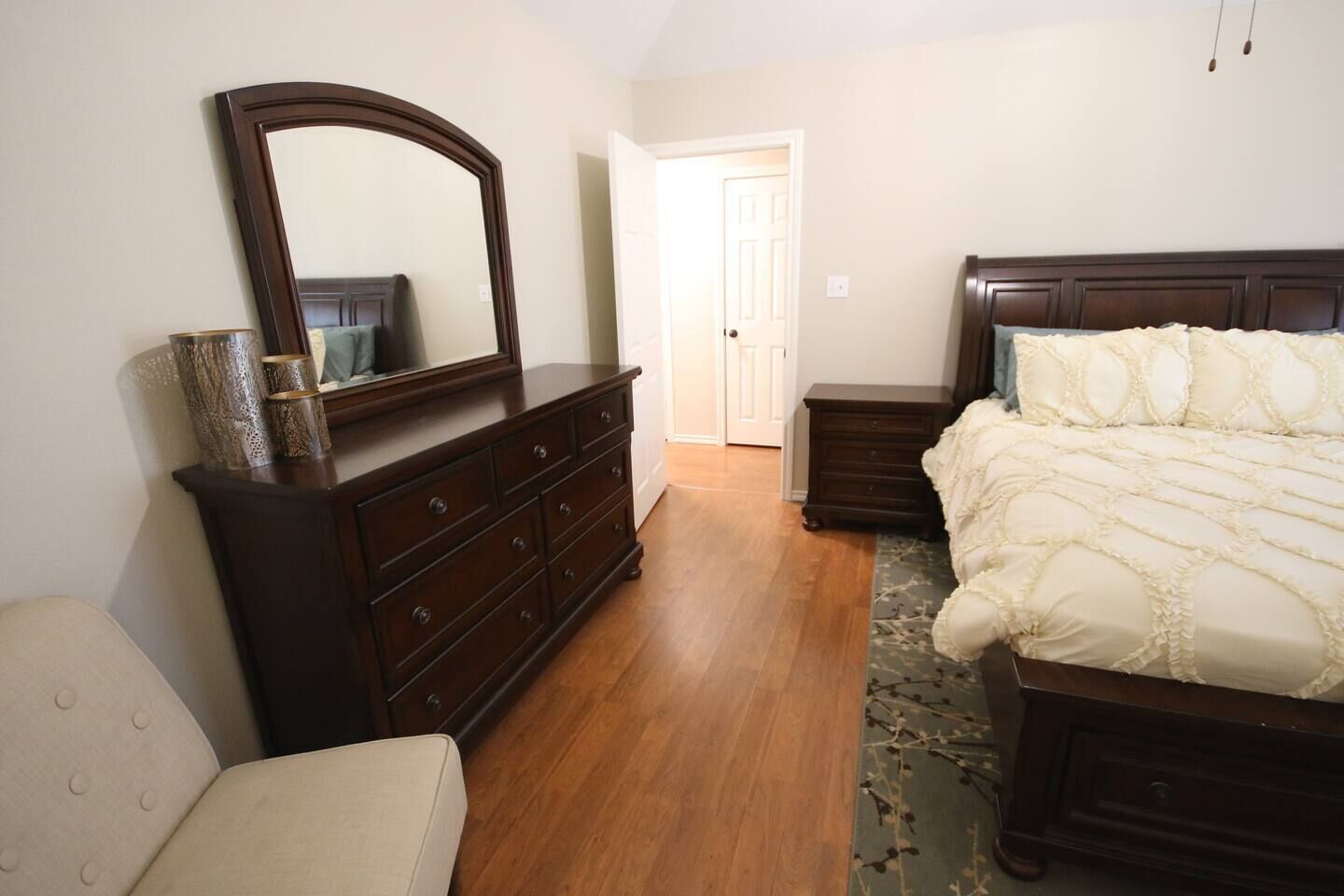 Un dormitorio con un espejo grande, una cama con ropa blanca, un aparador y una silla.