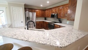 A kitchen with granite countertops, wooden cabinets, stainless steel appliances, and a black faucet. - Royal Entertainer - STAYeasttexas (Chandler)