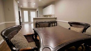 Un coin repas avec une grande table et six chaises, une cuisine à l’arrière-plan et un couloir menant à une autre pièce.