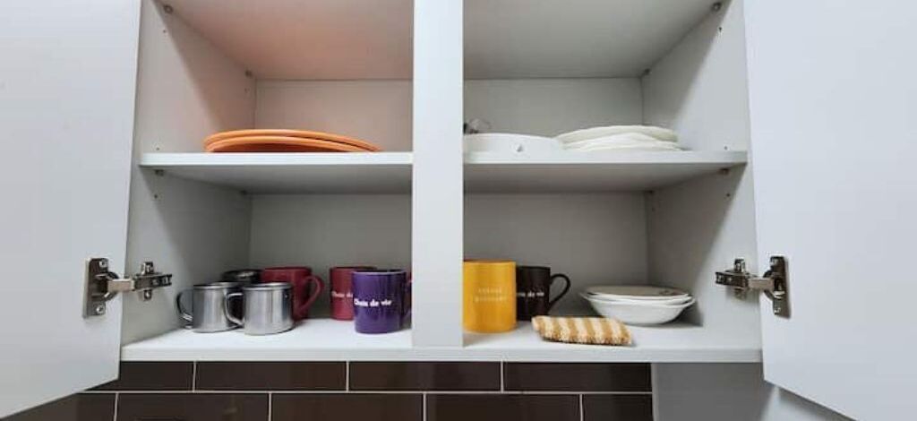A kitchen cabinet with shelves containing various kitchenware items.