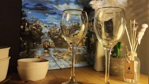 Deux verres à vin sont posés sur une table, avec un tableau et un chandelier en arrière-plan.