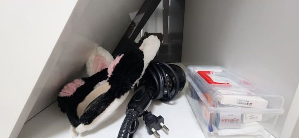 Un área de almacenamiento con un peluche blanco y negro, cables enrollados y recipientes de plástico con objetos.