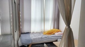 A small, single-bed room with a window, a curtain, and a yellow stuffed toy on the bed.