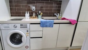 A compact kitchen with a built-in washing machine, a sink, and a countertop with kitchen utensils and a towel.