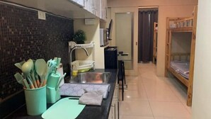 A compact kitchen with a sink, a countertop with kitchen utensils, a baby changing station, and a bunk bed in the adjacent room. - Sea Resi.MoA.Airport Netflix (Pasay)