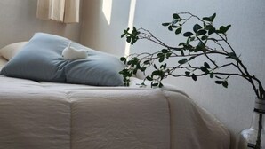 A neatly made bed with a light blue pillow and a white pillow, a vase with a branch of green leaves, and a window with curtains. - Daejeon Bedroom 3, Bathroom 2, Spacious Living Room Free Parking (Pasay)